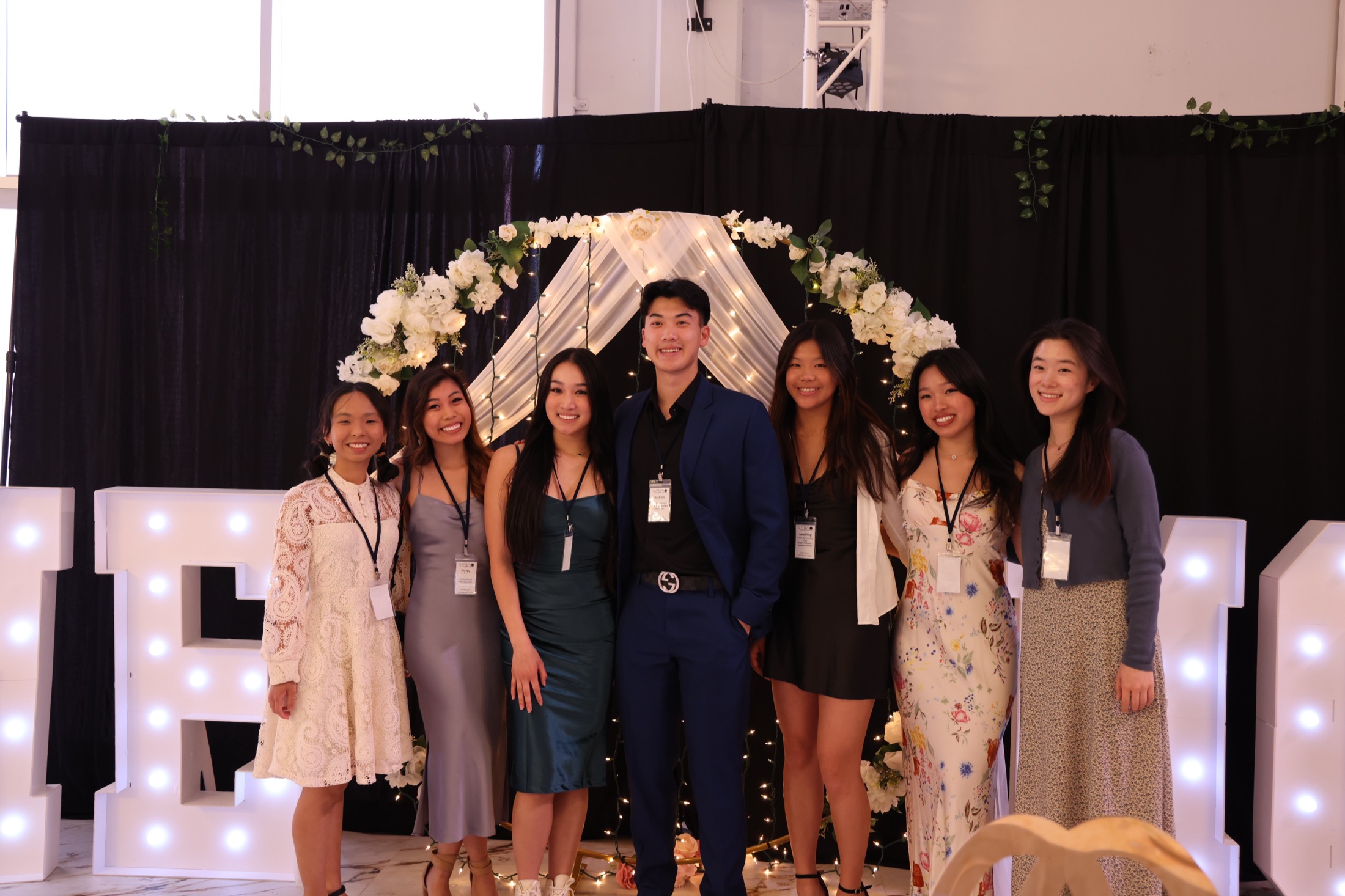 MEMO student leaders and supporters posing under the floral arch at the 2024 gala
